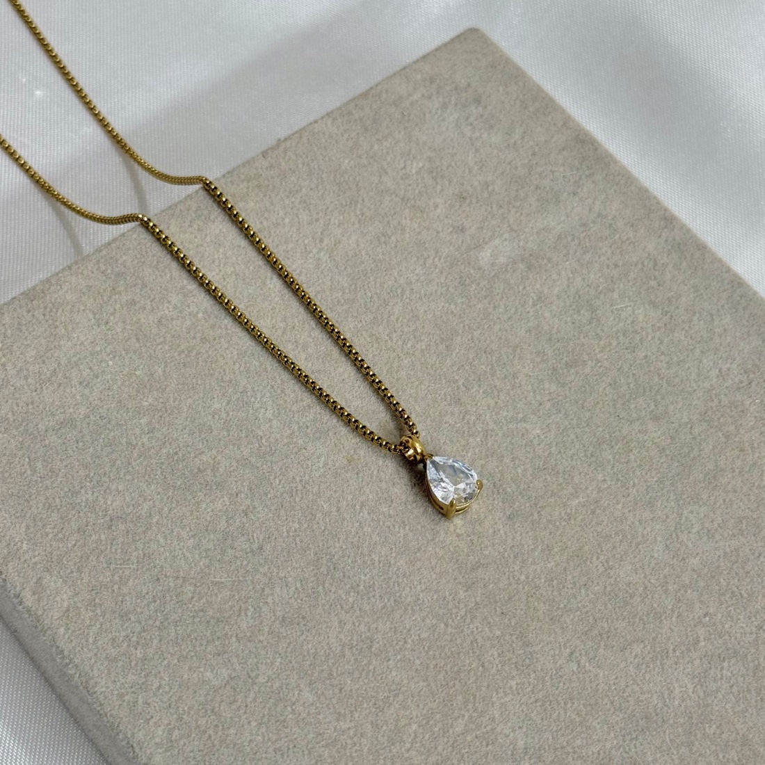Gold teardrop pendant photographed on a linen-covered stone